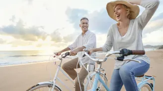 Man and woman in a hat riding bicycles on the beach at sunset. 