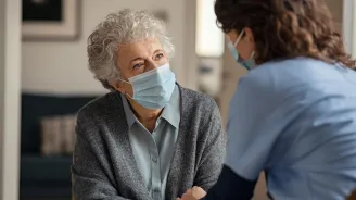 Hospice worker in mask, talking to elderly patient 