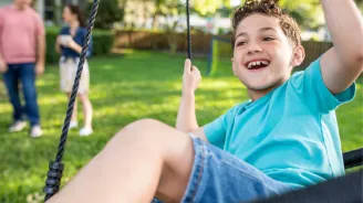 Boy on swing with parents in the background.