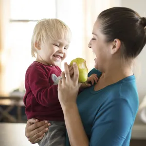 A Caucasian mom feeds her son a pear in the kitchen.