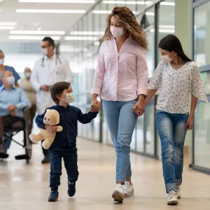 A Mother and Her Two Children Walk Hand and Hand Through a Hospital Hallway