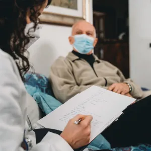 A doctor writing her notes down while talking with her senior patient