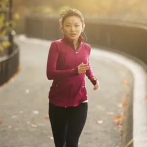 A young Asian woman jogs in the park on a fall afternoon.