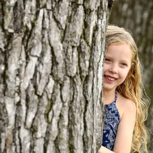 Girl Peeks Out From Behind A Tree