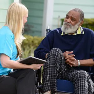 Elderly man in a wheelchair outside speaking to a nurse.