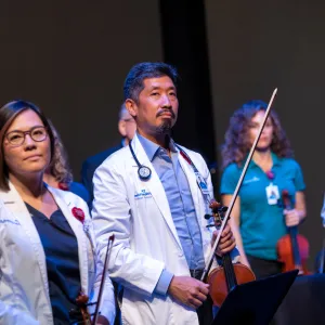 Wearing his white physicians coat, Dr. Vincent Hsu plays with the AdventHealth orchestra. 