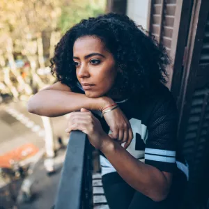 A Woman With a Concerned Look on Her Face Stares at Street From Her Balcony.