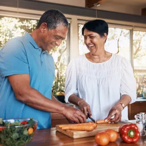 A couple cutting up carrots for a salad while in a kitchen.