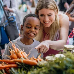 A young lady and a little boy pointing at carrots.