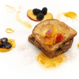three stacked slices of french toast, topped with a fruit sauce