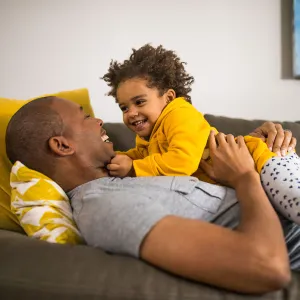 A dad is embracing his baby while they are laying down on the couch.