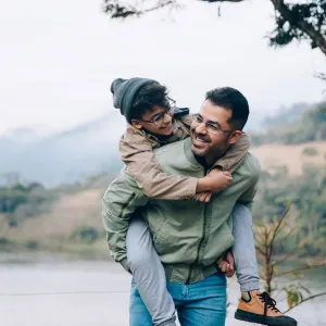 A father carrying his son on his back while hiking in the mountains