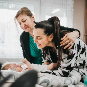 Grandmother and mother smiling at a baby laying on a bed.