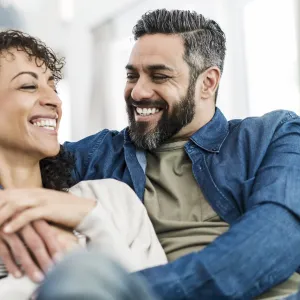 A couple laughing together on their couch at home.
