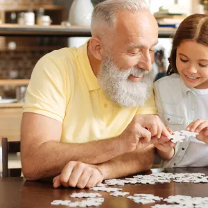 A grandfather puts together a puzzle with his granddaughter.