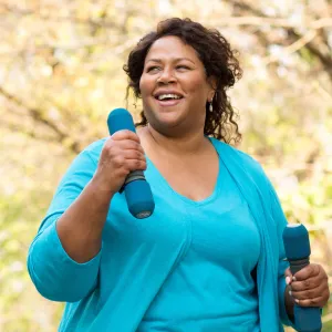 A woman exercising outdoors with hand weights.