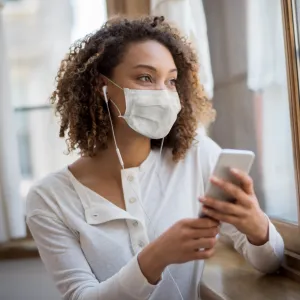 A woman wearing face mask and using her cell phone.