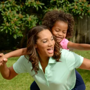 A mother carries her daughter on her back while playing outside. 