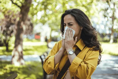 Woman blowing her nose into a tissue outdoors.