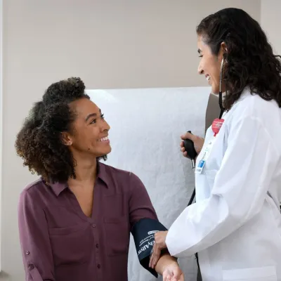 A young woman smiles at her doctor while getting her blood pressure measured.