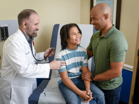 A Provider Checks a Child Patient's Breathing While His Father Supports Him