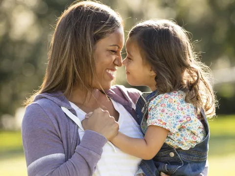 A mother smiles at her young daughter while holding her.