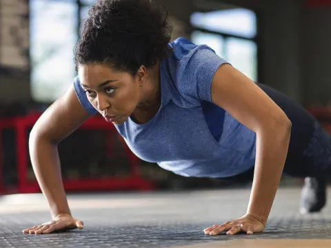 A young African American woman performs push-ups at the gym.