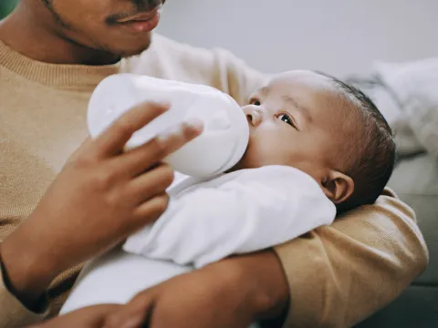 A Father Bottle Feeds His Baby Who is Swaddled in His Arms.