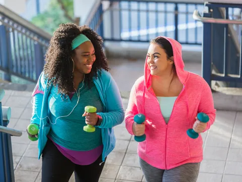 A Pair of Ladies, in Brightly Colored Clothing, Go Jogging in the City with Hand Weights.