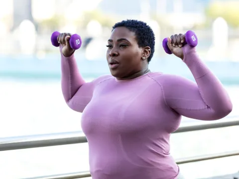 A Woman Exercises with Weights in a Park by the Water Front