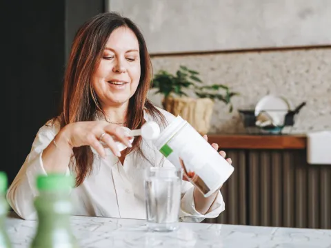 A Woman Scoops Protein Powder from a Container in Her Kitchen.