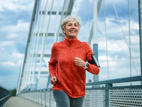 A Senior Woman Jogs Across a Bridge While Listening to Music