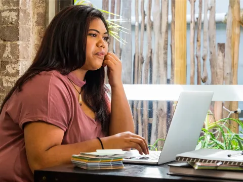 A Young Woman Sits at a Table and Surfs the Internet.