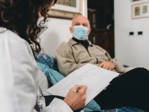 A doctor writing her notes down while talking with her senior patient