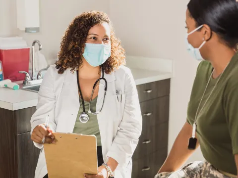A Doctor Speaks to Her Patient in an Exam Room While Wearing a Face Mask.