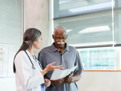 A Doctor Speaks to Her Patient in an Exam Room While Going Over His Charts on a Laptop.