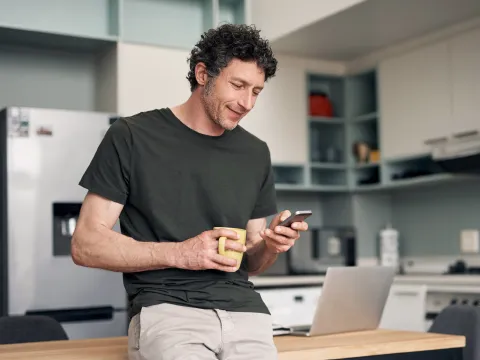 A Man Checks His Phone While Drinking His Cup of Coffee in a Kitchen