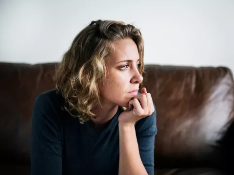 A Woman Sits in Her Home Staring Out the Window with a Serious Look On Her Face