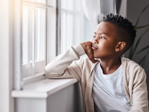 A Boy Stares Out the Window Bored in His Bedroom