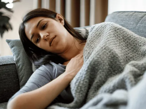 A Woman Lays on Her Couch With Her Hand on Her Chest