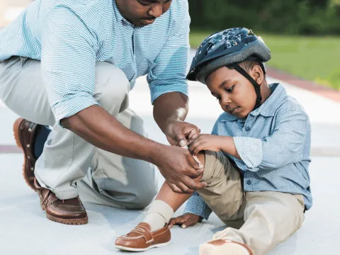 A Boy and His Father Tend to His Knee After Taking a Spill on a Bicycle