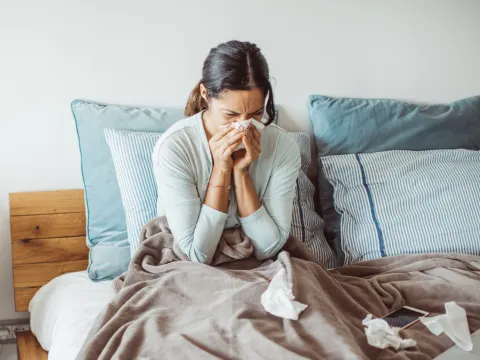 A Woman Blows Her Nose While Sitting Up in Bed