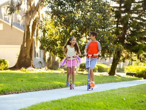 A brother and sister ride scooters through neighborhood