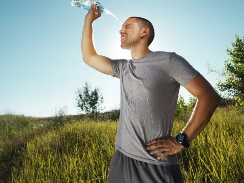 A man outside, post run, squirting water on his face