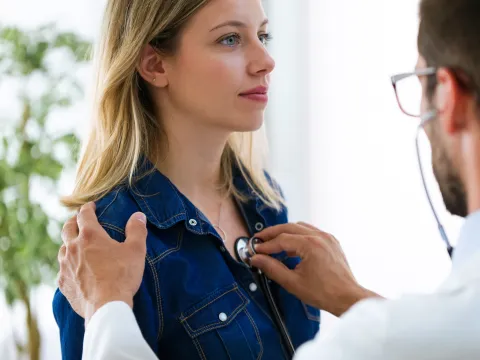 Doctor listening to woman's heart, a hand on her shoulder and a stethoscope