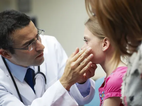 A male doctor examines the eyes of a young girl.