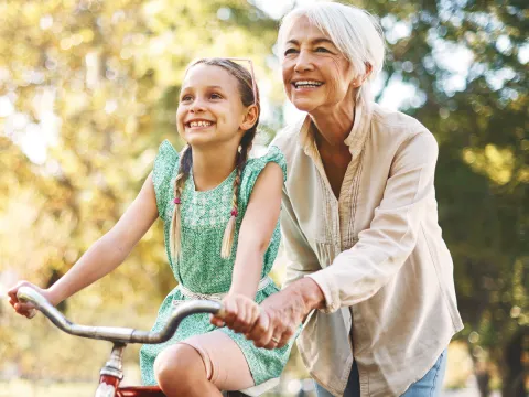 A grandmother helps her granddaughter ride a bike.