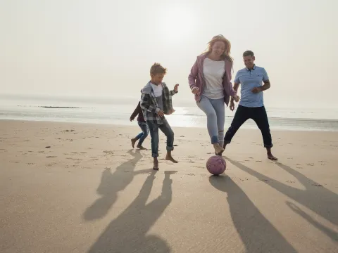 A family plays a friendly game of soccer on the beach