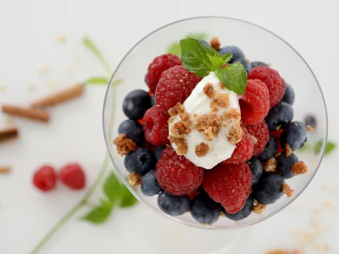 a clear glass bowl filled with creamy yogurt and a mix of berries, granola and topped with mint leaves