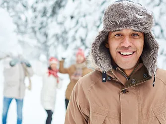 A group of people in snow, with a man at the forefront in focus in a brown jacket with a hod.